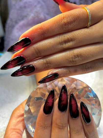 A close-up of the black and red ombré stiletto nails, highlighting the seamless blend of colors.