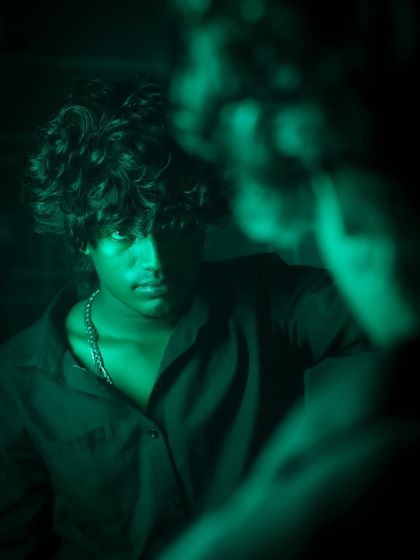 A creative mirror shot using green lighting. The reflection is blurred, drawing focus to the subject's intense expression and creating a theme of introspection or facing an inner self.