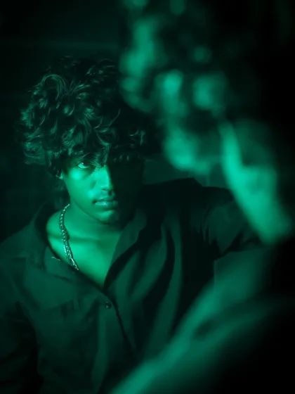 A creative mirror shot using green lighting. The reflection is blurred, drawing focus to the subject's intense expression and creating a theme of introspection or facing an inner self.
