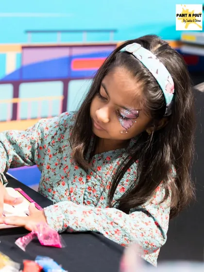 Art is for everyone. Here, a young participant is completely focused on her craft project at one of our carnival stalls, with some of our butterfly face paint art adding to the fun.