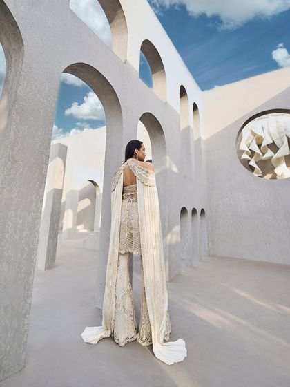 An ivory sharara set where light meets elegance. It features cold shoulder cuts, floor-sweeping sleeves, and intricate embroidery that reflects every shade of grace.
