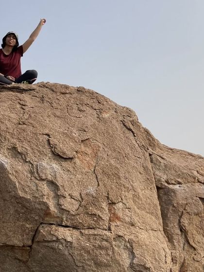 Sudha celebrating at the top of a boulder, a picture of pure joy and accomplishment.
