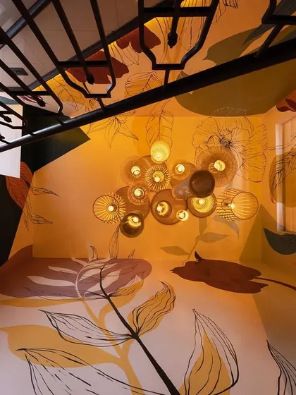 A view from the top of the yellow-themed staircase, looking down at the cluster of bamboo pendant lights. The artwork flows seamlessly across the walls and ceiling, enveloping the space in color and pattern.