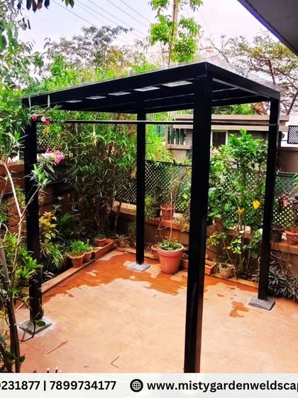 The finished pergola structure stands elegantly in a lush garden setting. The minimalist black frame provides a modern contrast to the natural surroundings, creating a perfect backyard retreat.