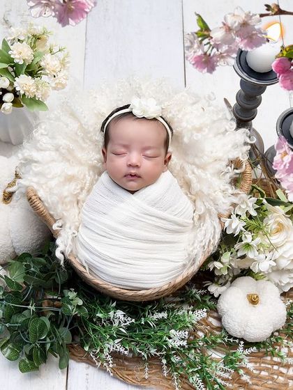 A baby sleeps in a basket surrounded by beautiful pink cherry blossoms. This setup is perfect for a soft, delicate, and spring-inspired newborn photo.