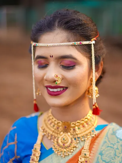 A close-up shot to appreciate the artistry of the bridal look. This photo highlights the detailed makeup, the traditional bindi, and the intricate design of her gold necklace and mundavalya. It’s a celebration of bridal beauty.