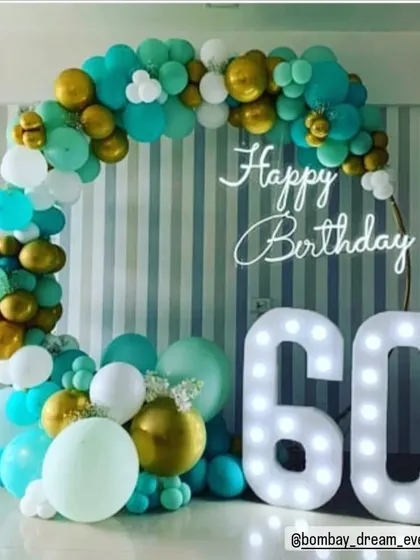 A chic and modern ring decor for a 60th birthday. The teal, white, and gold balloon arrangement is complemented by a neon "Happy Birthday" sign and large marquee numbers, creating a stylish and celebratory vibe.