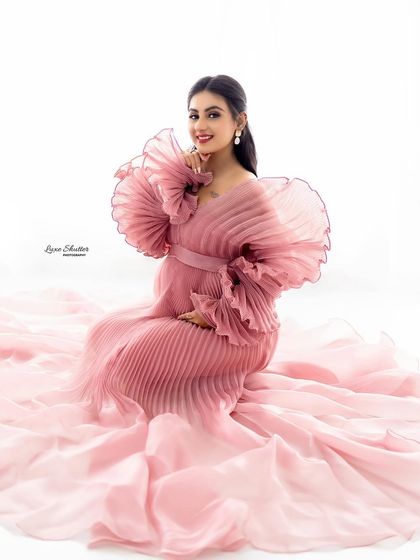 Seated poses allow the gown's fabric to pool around you like a cloud. This shot captures a moment of joyful anticipation in a sea of soft pink organza.