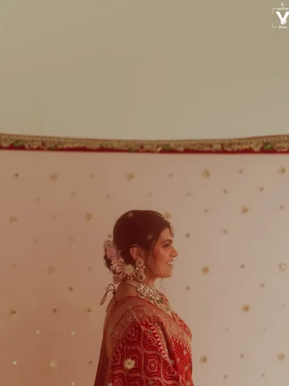 A profile shot of the bride in her beautiful red bandhani lehenga. The simple background and her elegant posture create a timeless and graceful portrait.