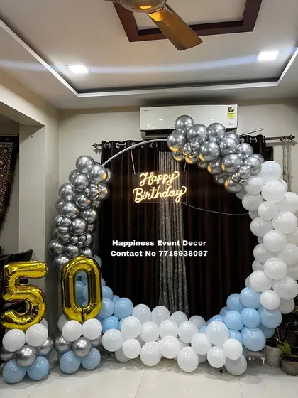 Even in a smaller space, a balloon ring can make a big impact. This setup for a 50th birthday was done at home, featuring a silver, white, and blue balloon arch with a neon sign and foil number balloons.