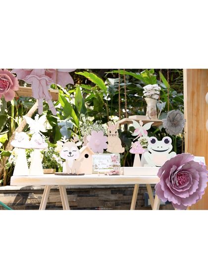 A table displaying various woodland and fairy-themed props, including cutouts of a fox, a bunny, a frog, and delicate paper flowers.