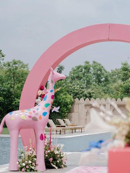 A whimsical pink giraffe with colorful spots stands by the pool, a key feature of this playful and imaginative carnival-themed decor.