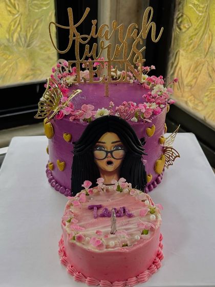 A unique "blow away" cake design for a mother-daughter celebration. The larger cake features a fondant face, and the smaller one is ready for the birthday wish.