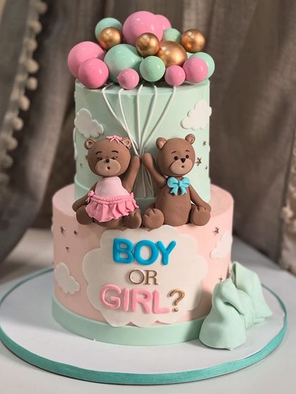 Boy or Girl? This adorable two-tier gender reveal cake features cute teddy bears, pastel pink and blue tones, and floating balloon toppers for a sweet and surprising announcement.