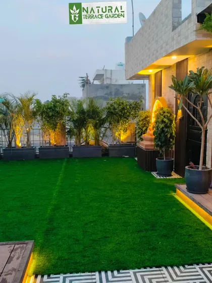 A wide view of a completed terrace in Uttam Nagar, showing the artificial lawn, planters with uplighting, and a seating deck.