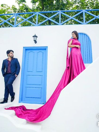A vibrant, Santorini-themed shot with the couple posing on white steps, the bride's magenta trail gown flowing down for a colorful and stylish look.
