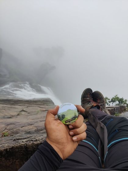 A trekker relaxes at the top of the falls, holding our Bandaje badge.