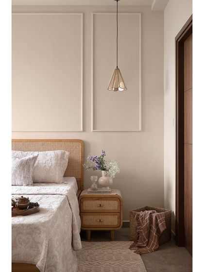 This guest bedroom embraces simplicity with subtle trim moulding on the walls, a cane headboard, and matching cane-front nightstands. Glass cone pendant lights add a touch of vintage charm.