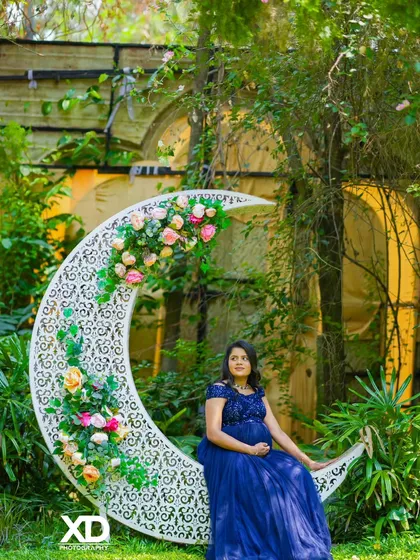 A dreamy solo portrait of the mother-to-be sitting on a floral crescent moon prop in a garden.