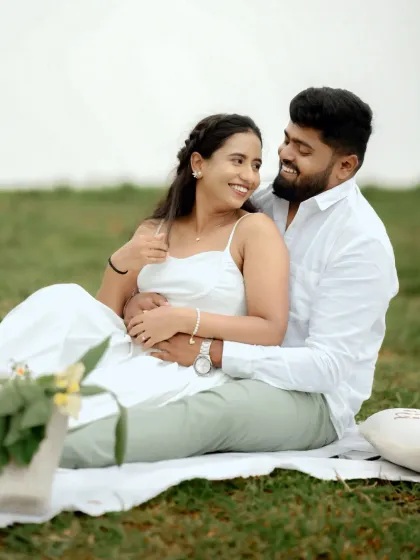 A candid and happy moment between a couple during a picnic-style pre-wedding shoot in a green field.