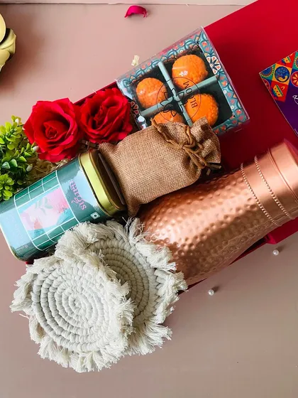 A top-down view of the red flap-open box, showing the rich texture of the hammered copper bottle and the handcrafted macrame coasters.