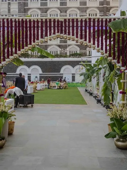 The entrance to Vijayshree and Omkar's wedding, featuring an arch of hanging purple flowers and brass bells. The path is lined with banana trees and traditional decor, creating a grand and auspicious welcome.