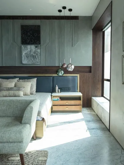 A sunlit view of the master bedroom in Kolkata, as seen in Elle Decor. The design highlights the textural contrast between the etched stone wall, wood paneling, and soft furnishings.