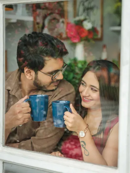A cozy coffee date moment, viewed from outside a window. This intimate shot captures the couple sharing a quiet conversation, creating a feeling of warmth and connection.