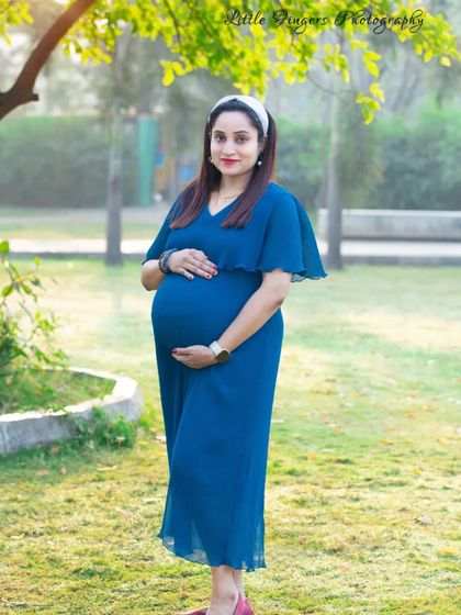 A full-length view of a stylish mom-to-be in a blue dress. The soft green lawn and trees provide a perfect, simple backdrop for this portrait.