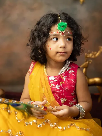 A thoughtful portrait of a little girl in her Radha costume, surrounded by festive props.