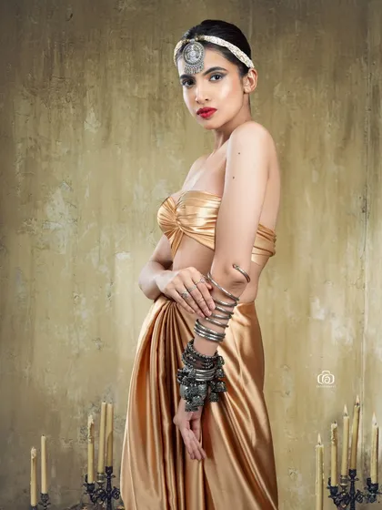 A side profile of a model in a golden satin outfit, highlighting the traditional silver headpiece and bracelets. The textured background adds a rustic feel to this fusion portrait.