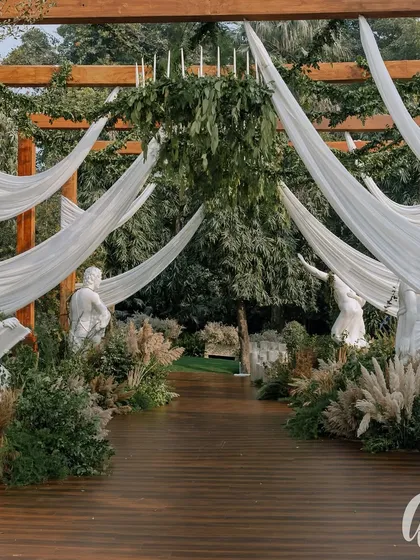 The guest's journey begins at the entrance. For this ivory garden wedding, we created a dramatic entryway with flowing white drapes, classical statues, and lush greenery, setting a tone of timeless elegance from the very first moment.