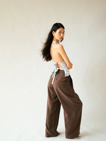 A fashion shot that plays with movement. The slight motion blur in the hair adds a dynamic quality to this full-length look, highlighting the silhouette of the wide-leg pants and backless top.