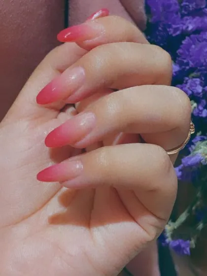 A classic red ombre effect on sharp, almond-shaped nail extensions, blending from a sheer nude base to a vibrant red tip for a seamless gradient look.