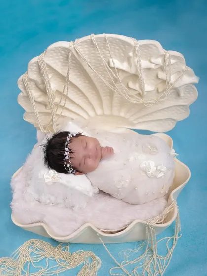 A serene portrait of a newborn nestled in our seashell prop. The soft white fabrics and simple blue background create a dreamy, ocean-inspired atmosphere for this creative baby photoshoot.