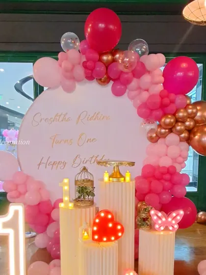 A closer view of the pink and rose gold first birthday decor, focusing on the cake stands and the beautiful balloon color combination.