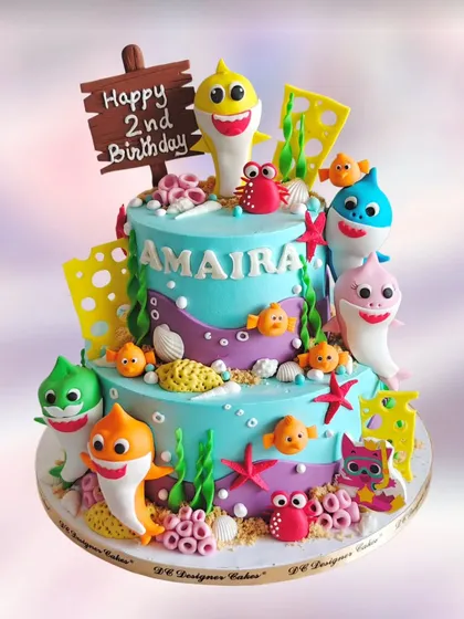 A vibrant two-tier Baby Shark cake for a second birthday. The cake is decorated with the entire shark family and other sea creatures, creating a fun underwater scene.