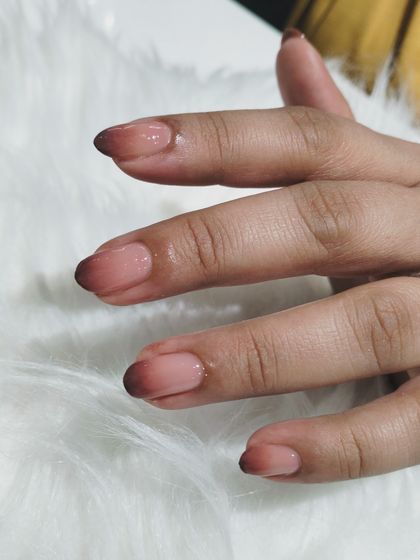 A moody and sophisticated ombré on short, natural nails, blending from a sheer nude base to a deep brown, almost black, tip.