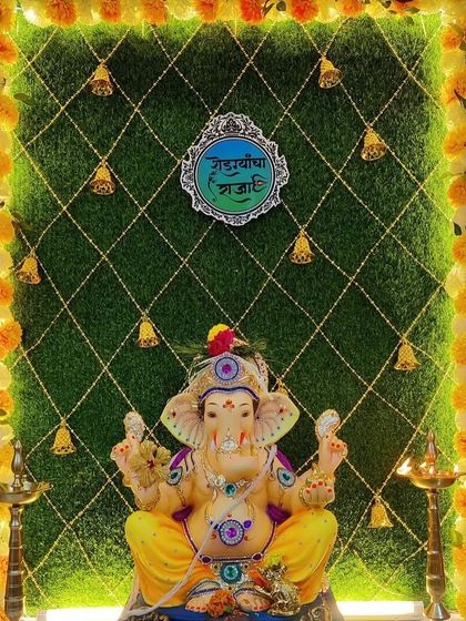 A creative Ganpati backdrop using a green turf wall with a crisscross pattern and hanging bells. The frame of marigold flowers adds a traditional touch to this unique design.