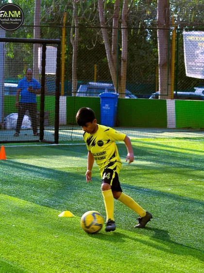 A young player focuses on the ball during a dribbling exercise in the bright sunlight.