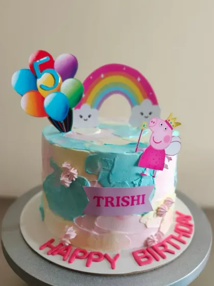 A colorful Peppa Pig cake with a rainbow and balloon toppers. The pastel watercolor effect on the buttercream is a fun touch.