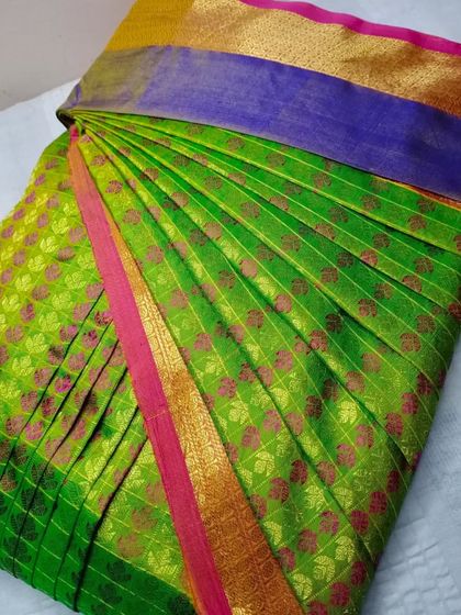 A bright green saree with a purple and gold border. The pleats are done to perfection, ready for a festive celebration.