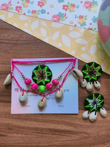A vibrant and bohemian-style Navratri set. This piece combines neon pink and green threadwork with a central mirror pendant and cowrie shell details for a modern twist on festive jewelry.