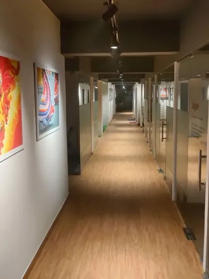 This corridor in a co-working space in Noida is designed to be clean and functional. We used wood-look flooring for warmth and durability, while the walls are lined with vibrant, large-scale art prints to energize the passage between private office cabins.