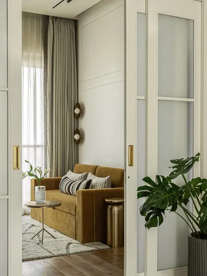 This cozy den room doubles as a guest space, with a mustard-toned sofa bed and a cylindrical bar unit. Sliding doors with switchable glass open to a sunlit area, making the room feel airy and versatile.