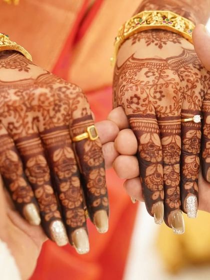 A close-up of a couple holding hands during their engagement, showing the bride's delicate mehendi.