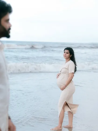 This shot captures the mother-to-be looking back towards her partner, her hand resting on her bump. It tells a story of partnership and the shared journey of pregnancy against the beautiful ocean backdrop.