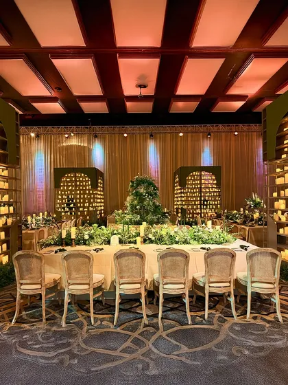 A long dining table set for an intimate feast, surrounded by candle walls and featuring a lush floral runner, creating a warm, glowing, and opulent atmosphere.