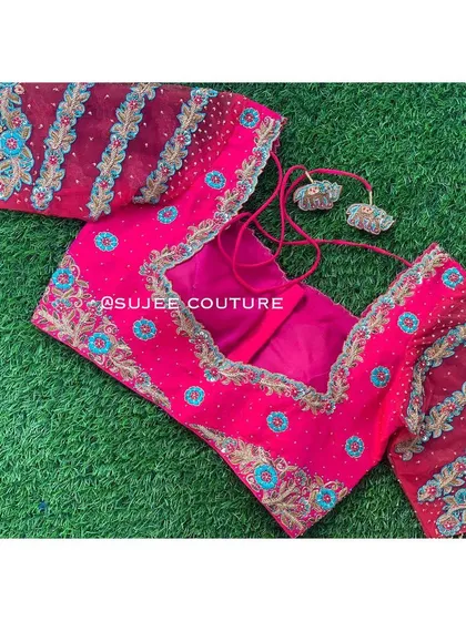 A bright pink blouse with sheer, striped sleeves. The body and sleeves are embellished with blue and gold floral motifs, and it features a deep, open back design.