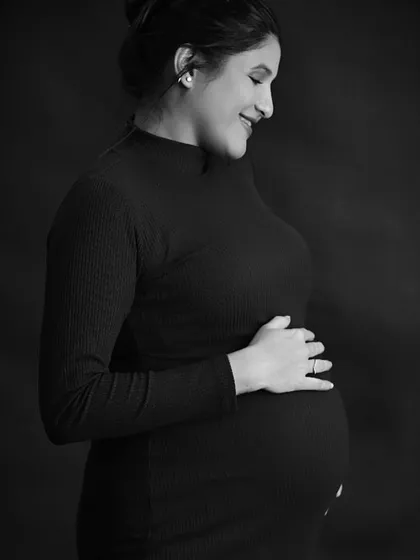 An elegant solo maternity portrait in black and white, with the mom-to-be cradling her bump against a dark background.
